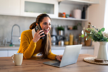 Happy satisfied businesswoman using modern smartphone and laptop in her home office at early...