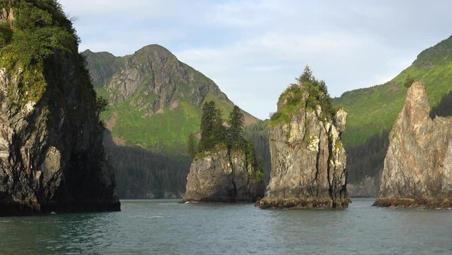 ALASKA - 2023 - View from a kayak as it approaches giant green-topped rocks and mountains in Alaska's Resurrection Bay.
