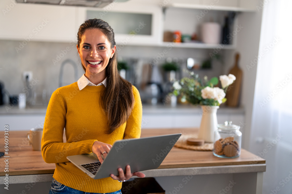 Wall mural Smiling confident businesswoman looking at camera standing at home. Home office. Modern stylish female corporate employee successful executive manager with laptop posing for business portrait.