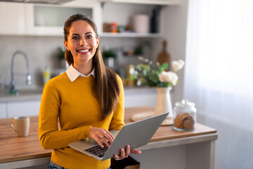 Young female freelancer or remote teacher using laptop looking at camera while working at home.