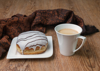 Delicious donut with chocolate on a white plate and a cup of coffee on a wooden table. Top view,...