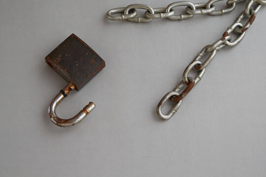 Opened padlock and broken chain on gray background. Break the shackles, gain freedom, fight for freedom.
