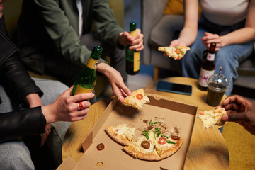 Close up shot of friends sitting relaxing at home sitting at small wooden table sharing pizza and...