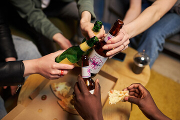 Close up shot of people hands toasting with beer bottles at home party with pizza