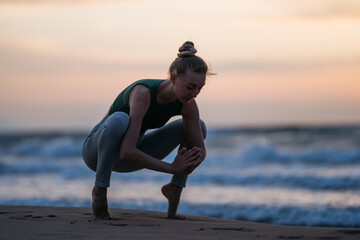 A serene silhouette of a woman gracefully flowing through yoga poses on the seashore as the sun...