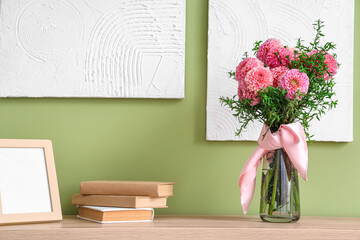 Vase of beautiful pink dahlias with books and frame on commode in living room