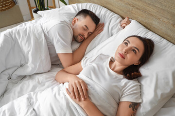 Awake young woman with her sleeping husband in bedroom