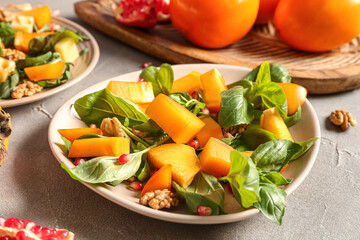Plate of delicious salad with persimmon, pomegranate seeds and walnut on grey background