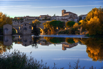 View of the city of Zamora and watermills and the San Pedro Church in the background in autmn at sunset reflected in the Duero river. Spain
