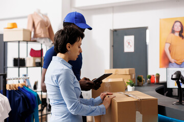 Store manager looking at packages with courier, checking boxes with shipping details in modern...