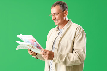 Mature man in eyeglasses reading newspaper on green background