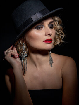 Sexy fashionable woman in an elegant hat and black dress. Mysterious blonde in retro style on a black background.