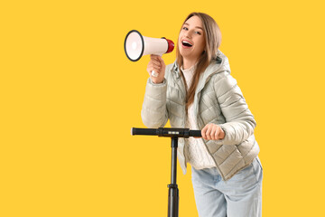 Young woman with electric scooter shouting into megaphone on yellow background