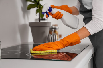 Female janitor cleaning electric stove in kitchen, closeup