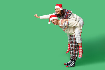 Happy young couple in Christmas pajamas having fun on green background