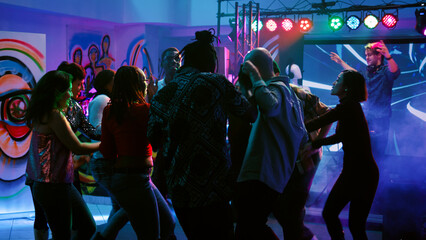 Diverse people having fun partying at club, dancing on live music performance with colorful glowing...