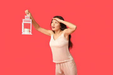 Beautiful young Asian woman in pajamas with lantern on red background