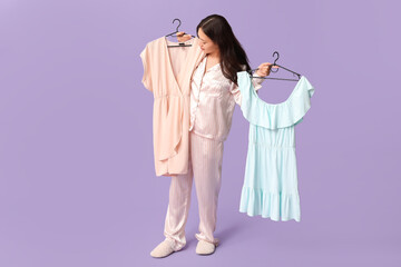 Beautiful young Asian woman in pajamas with different dresses on purple background