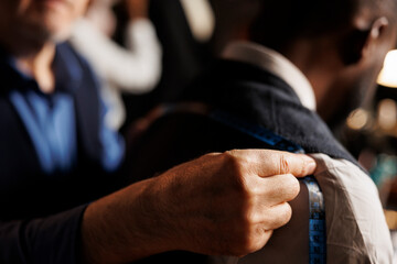 Close up of professional experienced suitmaker doing fitting length estimations on sartorial piece...