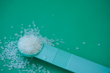 White sugar on the measuring spoon isolated on green