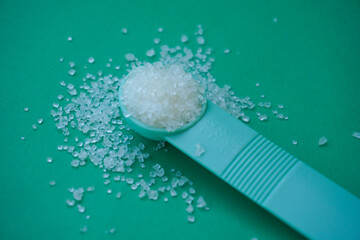 White sugar on the measuring spoon isolated on green