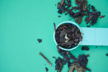 dry tea leaves in a measuring spoon to make a cup of tea isolated on green background