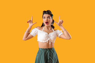 Attractive pin-up woman pointing at something on yellow background