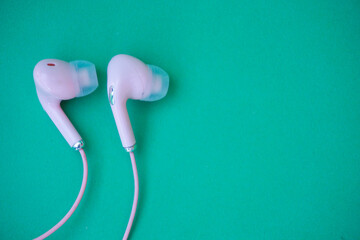 Pink wired earphones isolated over green - obrazy, fototapety, plakaty