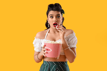 Scared young pin-up woman with popcorn on yellow background