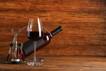 Bottle and glass of red wine with corkscrew on wooden background