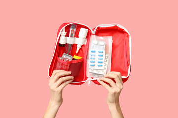Female hands holding first aid kit with pills and medicine bottles on pink background