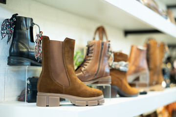 Closeup of stylish demi-season brown suede and leather womens boots on shelves in modern footwear store. Comfort and fashion concept