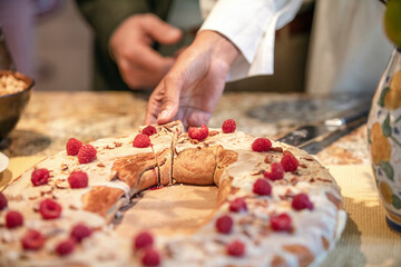 A woman reaches and takes a slice of delicious bread based pastry covered in raspberries and almonds at a wedding reception and tea