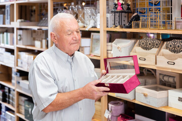 Portrait of positive mature man searching box for jewelry storage at store