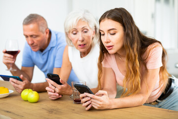 Elderly parents and adult daughter surf the internet using mobile phones in the kitchen