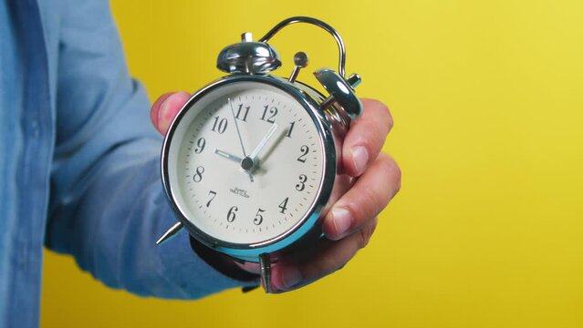Man gesturing with his hands with a classic alarm clock on an isolated yellow 