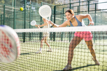 Dynamic young woman playing Padel Tennis with partner in the open air tennis court