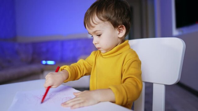 Serious cute Caucasian kid focused on drawing. Portrait of a lovely baby boy having fun at home.
