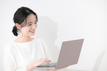 笑顔でノートパソコンを見るオフィスカジュアルの若い女性　白バックの上半身　右にコピースペースあり