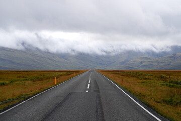 Empty road leading to green tall cloudy mountains