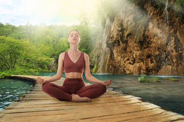 Woman meditating on wooden bridge near river in mountains