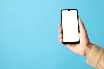 Man holding smartphone with blank screen on light blue background, closeup. Mockup for design