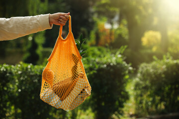 Conscious consumption. Woman with net bag of eco friendly products outdoors, closeup. Space for text
