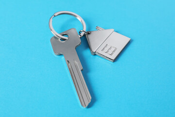 Metallic key with keychain in shape of house on light blue background