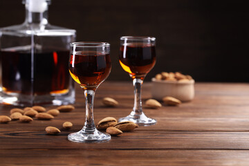 Liqueur glasses with tasty amaretto and almonds on wooden table, closeup. Space for text