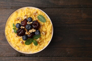Tasty cornmeal with blueberries, dates, walnuts and mint in bowl on wooden table, top view. Space for text