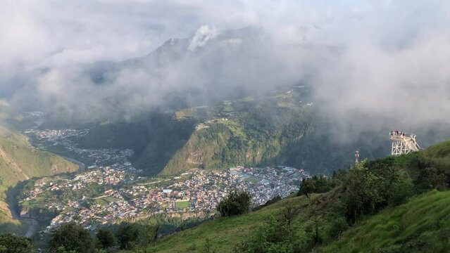 Tourists take photos at Baños viewpoint with a view of Tungurahua volcano in the clouds
