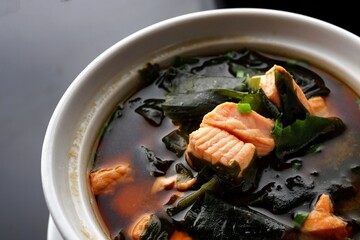 Miso soup with salmon, seaweed and onions, on a black background