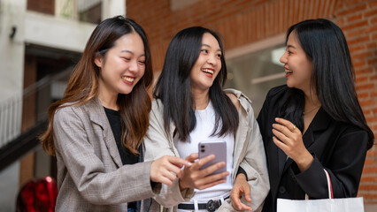 Beautiful Asian women are looking at a phone screen with happy faces, shopping in the city together.