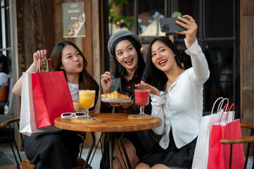 Group of attractive Asian female friends are taking selfies while hanging out at a cafe together.